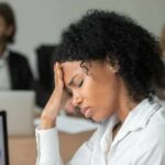 Adrenal Fatigue Debunked – The Stress Alarm That Won’t Shut Off Woman in office holding her head with eyes closed