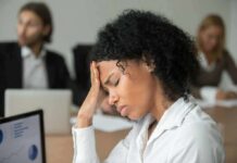 How To Manage Stress and Build Resilience Easily Woman in office holding her head with eyes closed