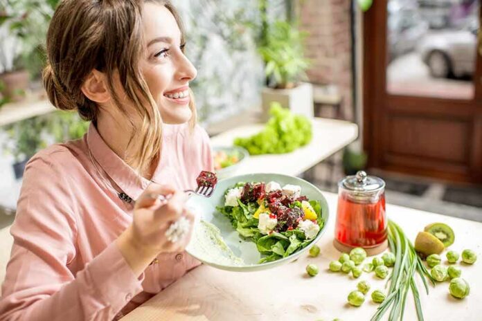 shutterstock_1028139997 Woman eating a fresh salad at a cafe table