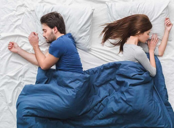 Couple sleeping back to back under a blue blanket