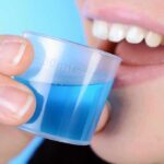 Dry Mouth Epidemic: Popular Meds Wreck Saliva person holding a small cup of blue mouthwash near their teeth