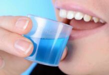 person holding a small cup of blue mouthwash near their teeth