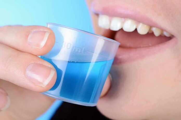 shutterstock_1065244808 person holding a small cup of blue mouthwash near their teeth