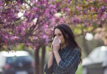 Woman sneezing into tissue under blooming pink trees