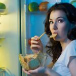 Woman snacking at an open refrigerator