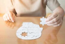 Person holding puzzle piece over head-shaped jigsaw on table