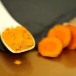 Toxic Lead Found In ‘Healthy’ Turmeric Turmeric powder on a white spoon beside sliced turmeric root