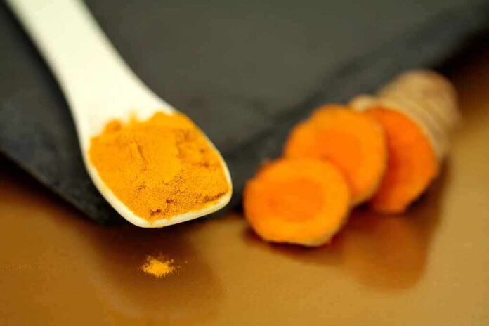 shutterstock_1310460299 Turmeric powder on a white spoon beside sliced turmeric root