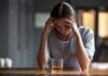 Heavy Booze, Darker Mind? Woman with head in hands at a bar with a glass of whiskey