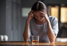 Woman with head in hands at a bar with a glass of whiskey