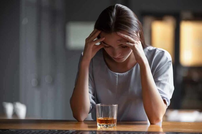 shutterstock_1492615838 Woman with head in hands at a bar with a glass of whiskey