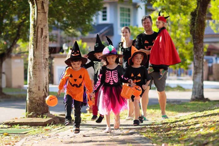 shutterstock_1499421917 Children in Halloween costumes trick-or-treating with adults on a sunny street