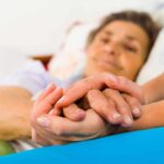 Caregiver holding hands with an elderly patient in bed