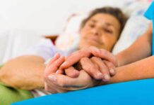 Terrifying Pattern Inside ‘Safe’ Nursing Homes Caregiver holding hands with an elderly patient in bed