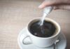 hand pouring sugar into a cup of black coffee