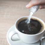hand pouring sugar into a cup of black coffee