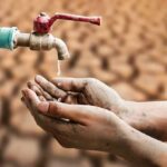 Hands catching drops from a faucet over parched ground