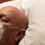 Elderly man wearing a face mask resting on a pillow
