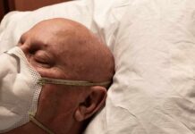 Elderly man wearing a face mask resting on a pillow