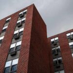 Brick apartment buildings with window air conditioners under cloudy sky