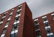 Brick apartment buildings with window air conditioners under cloudy sky