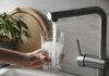 Filtered Tap Water: Lab Test Exposes What Filters Miss Hand holding a glass under a kitchen faucet