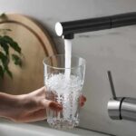 Hand holding a glass under a kitchen faucet