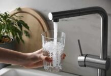 Hand holding a glass under a kitchen faucet
