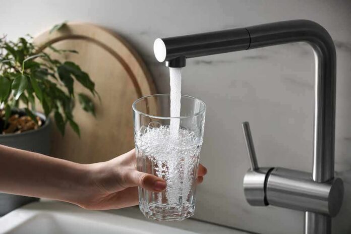 shutterstock_2247078069 Hand holding a glass under a kitchen faucet