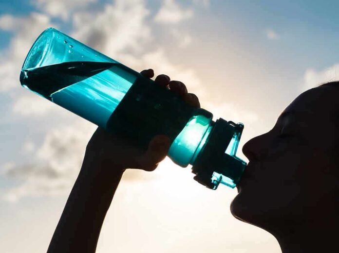 Silhouette person drinking from a blue water bottle