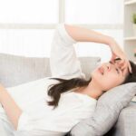 Woman lying on sofa with hand on forehead