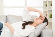 Woman lying on sofa with hand on forehead