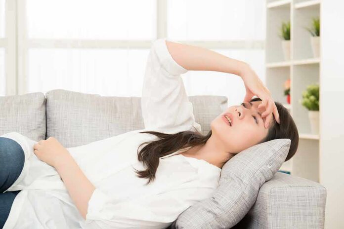 shutterstock_542943343 Woman lying on sofa with hand on forehead